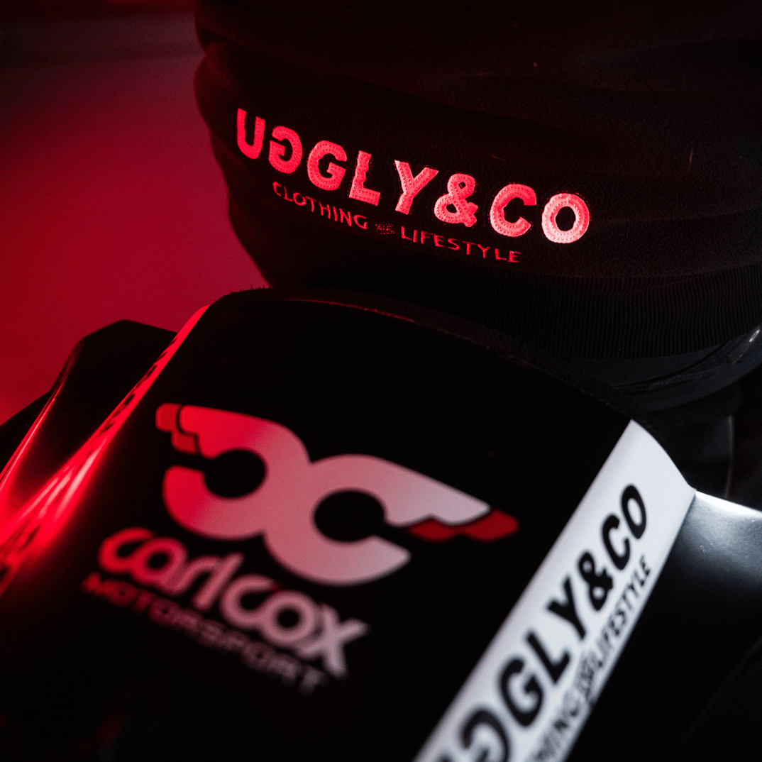 Close-up of a black jacket with 'Uggly&Co' and Carl Cox motorsport logos on a dark background