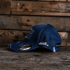 Left side view of a blue denim Baseball Cap with Uggly&Co branding and Mike Browne 16 logo on the side on a wooden background