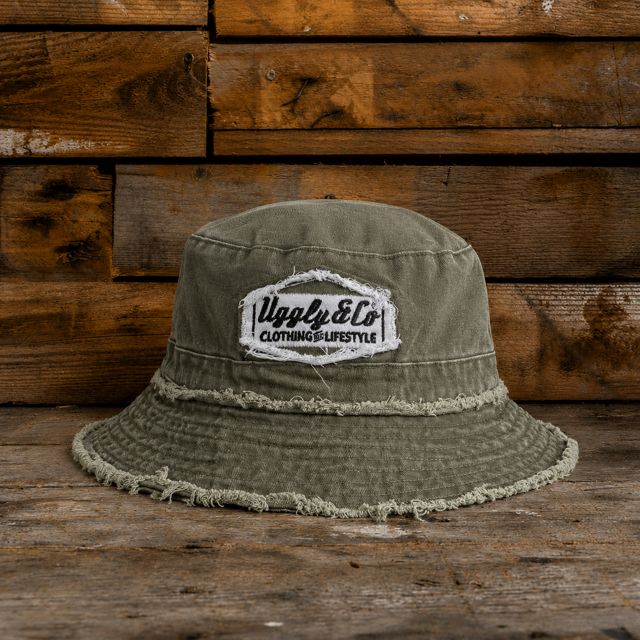 Frayed green bucket hat with an Uggly&Co diamond logo on a wooden background
