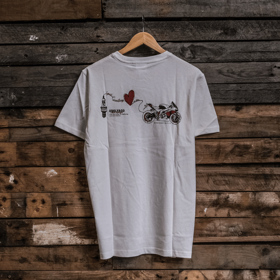 Rear view of a limited edition Valentine’s white t-shirt with spark plug heart graphic, and Uggly&Co logo on a wooden background