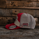 Side view of a red and beige trucker hat with Uggly&Co branding and a mesh back section on a wooden background