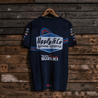 Rear view of a navy Team Classic Suzuki blue t-shirt with Uggly&Co branding on a wooden background