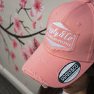 Close up detail of a female model wearing the Washed Pink Vintage Cap with a modified car behind her