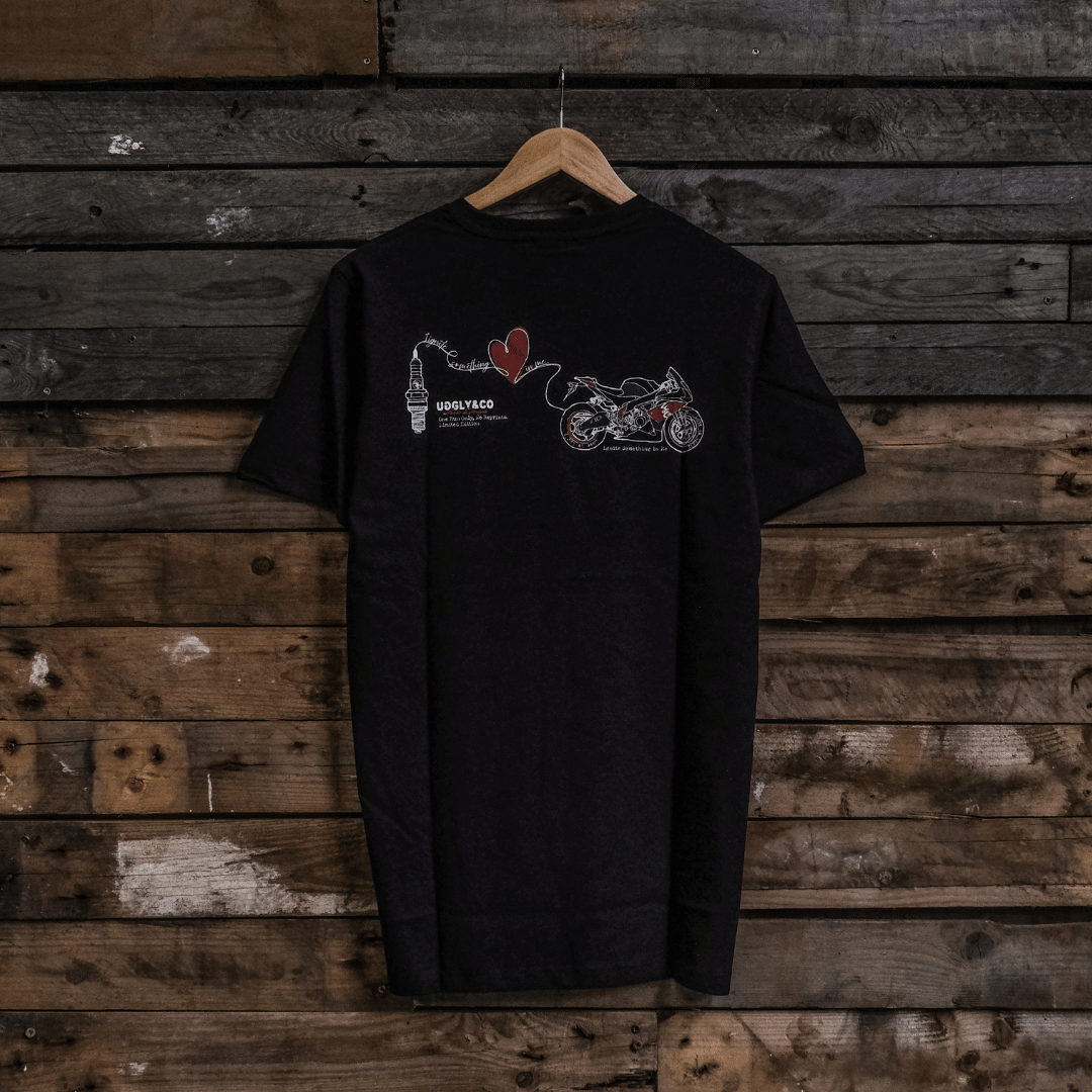 Rear view of a black t-shirt with a motorcycle, love heart and spark plug graphic on a wooden background