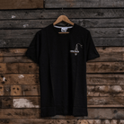 Front view of a black t-shirt with a spark plug graphic and the Uggly&Co logo on a wooden background